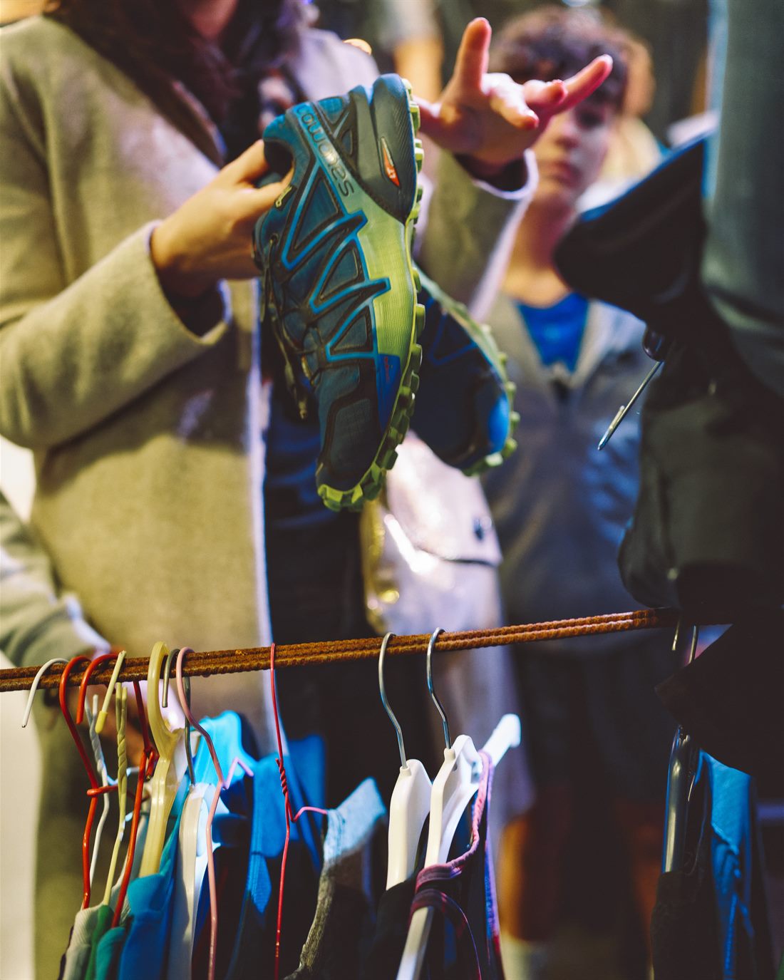 Une personne examine une chaussure de trail d’occasion au-dessus d’un portant de vêtements