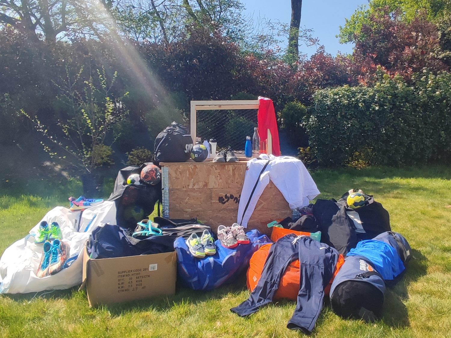 Matériel de sport collecté et trié en extérieur : sacs, chaussures, vêtements et équipements posés sur l’herbe
